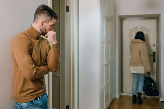 Frau verlässt nach der Trennung die gemeinsame Wohnung und Mann schaut ihr traurig nach
